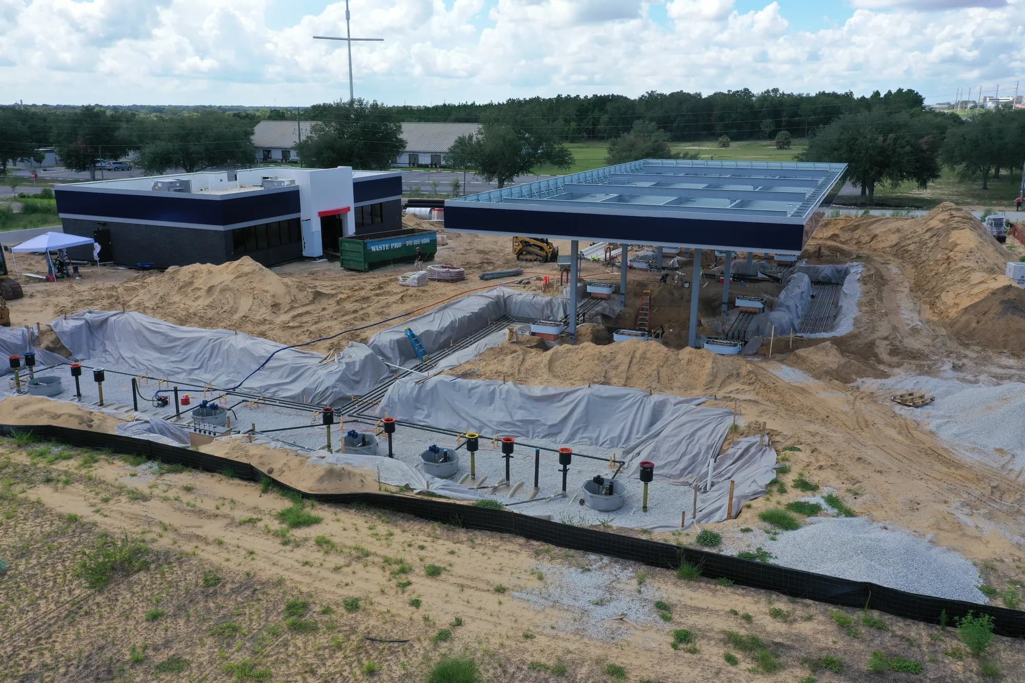 Aerial of a convenience store and fuel canopy under construction with an open underground tank excavation