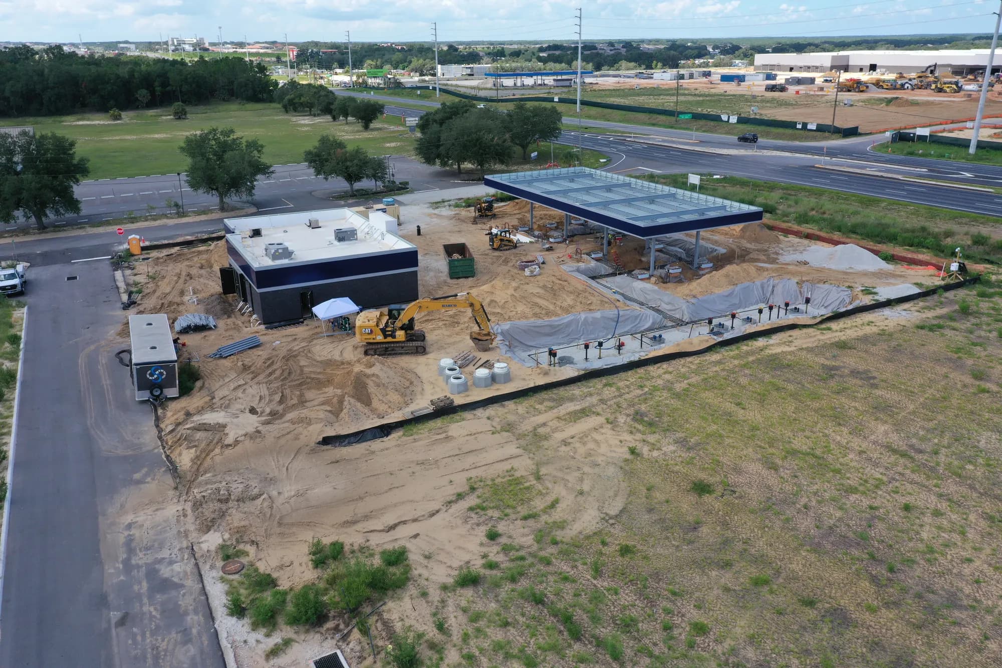 Aerial of a fuel station construction site with an excavator beside an open underground tank pit