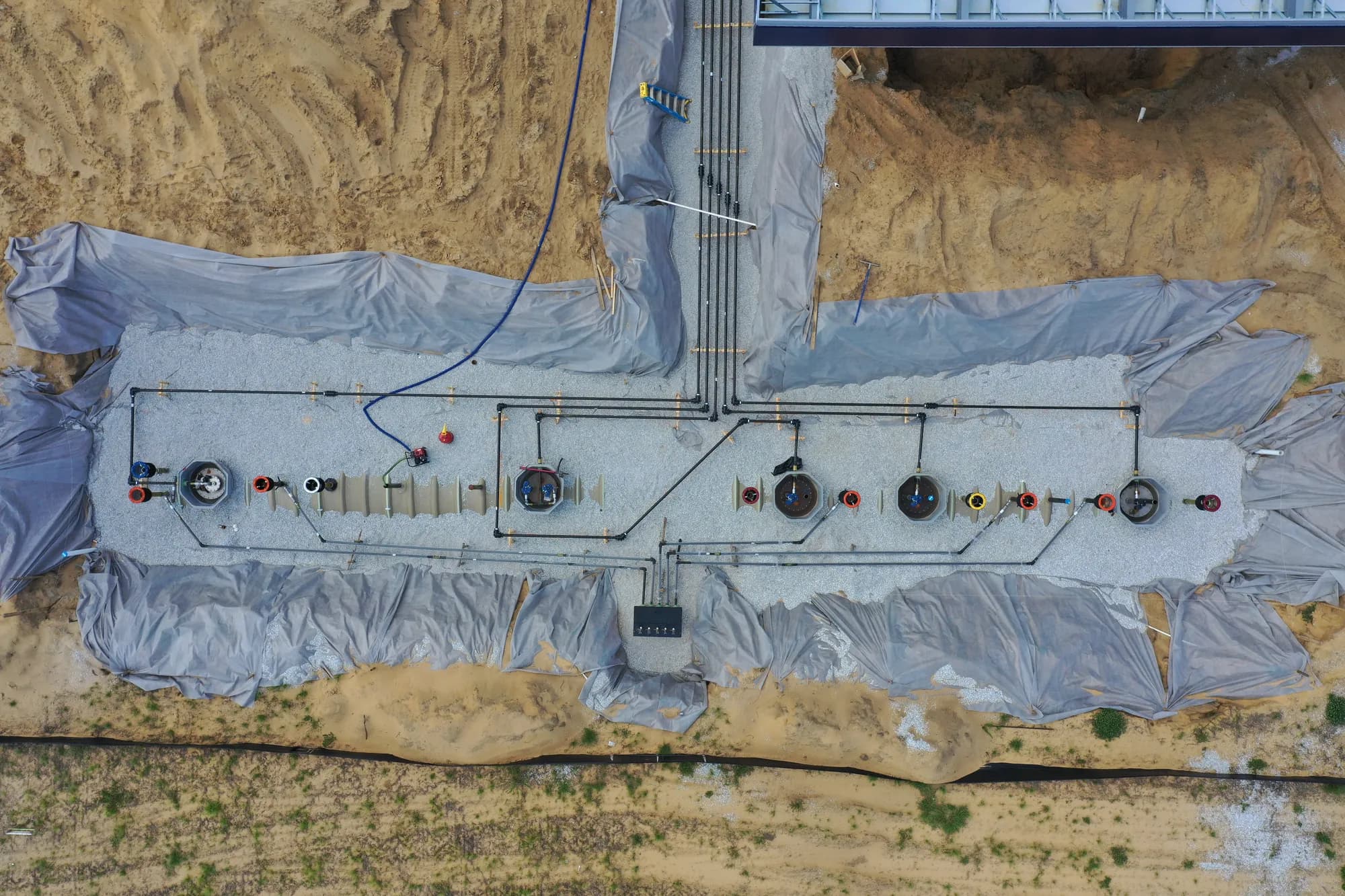 Top-down view of underground fuel tanks and piping laid out in a gravel-bedded excavation