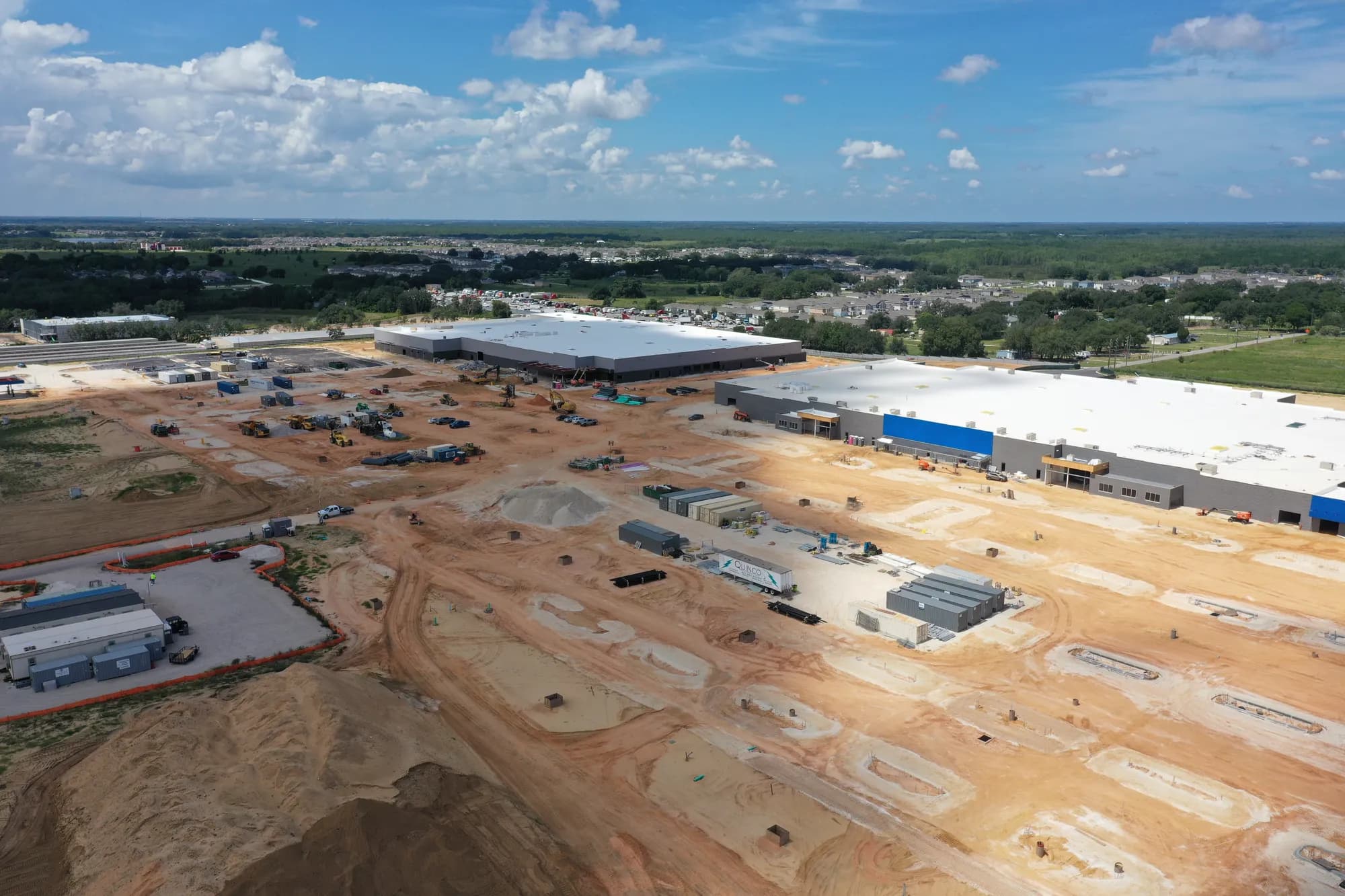 Oblique aerial of a roofed big-box retail building with graded site and construction equipment in front